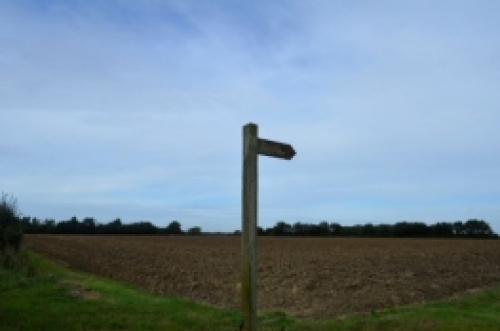 A wooden post indicating country path through fields